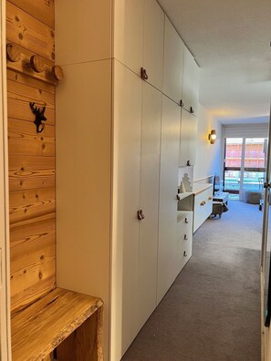 Un pasillo con paneles de madera en una pared, un armario blanco con varias puertas y un banco.