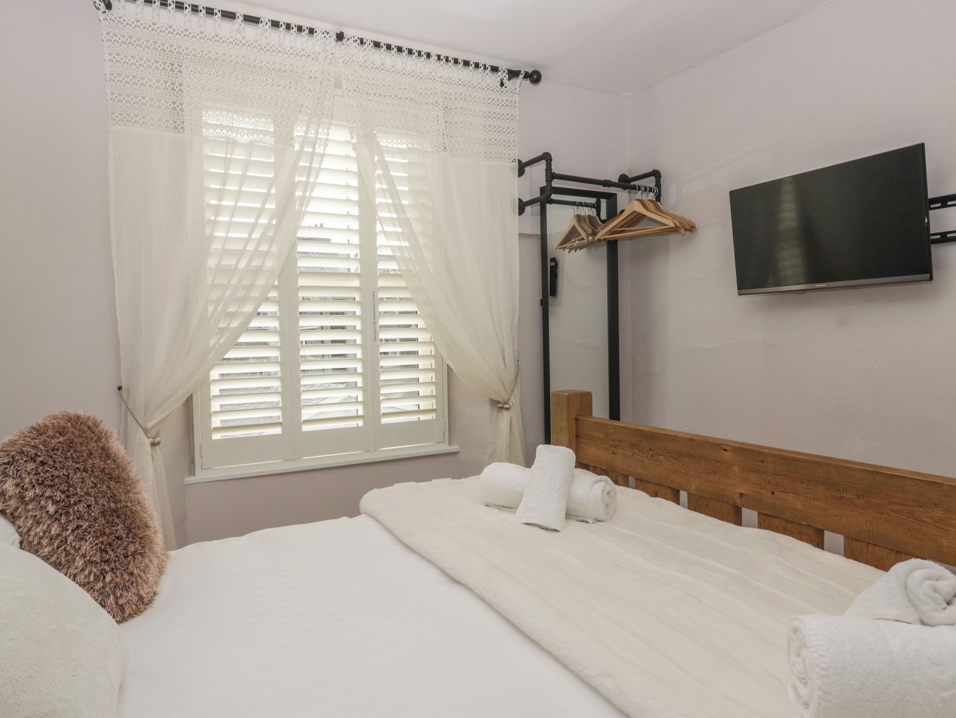 Una habitación de hotel con una cama, un televisor montado en la pared y una ventana con cortinas.