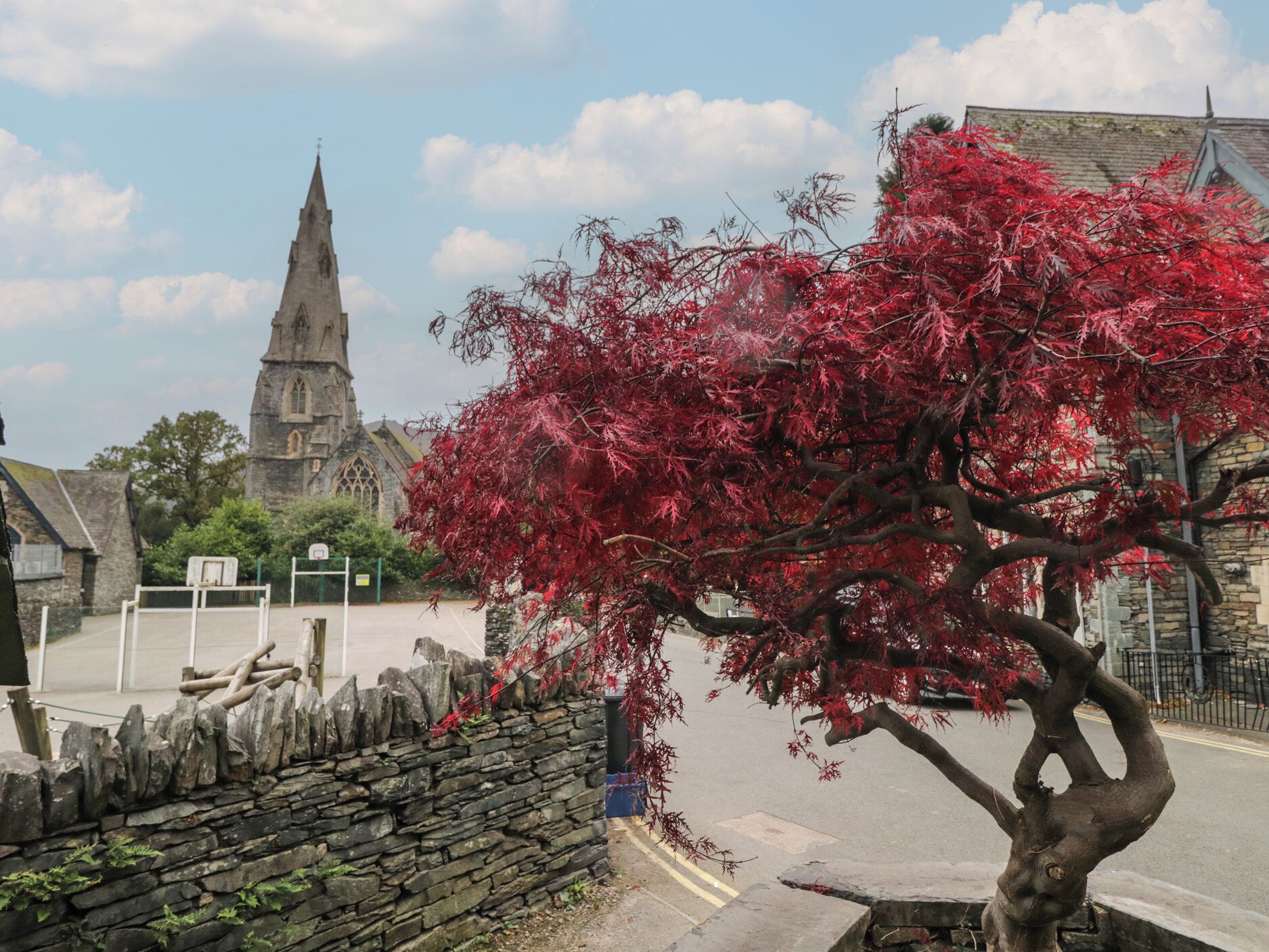 A stone wall, a tree with red leaves, and a church with a tall spire.