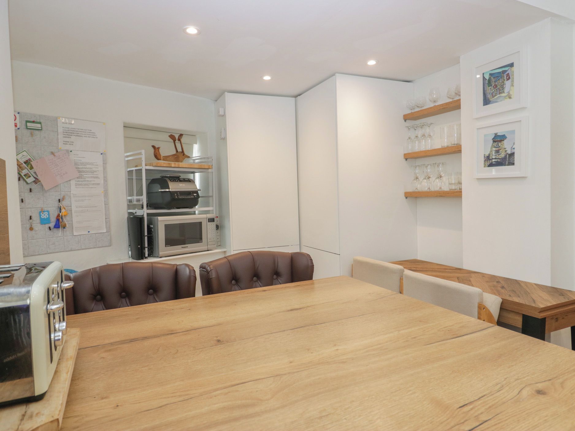 Una cocina moderna con una mesa de comedor de madera, dos sillas de cuero, horno empotrado y refrigerador.