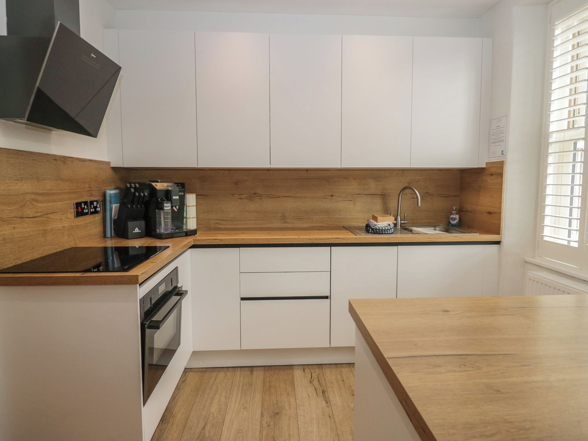 Une cuisine moderne avec des meubles blancs, un plan de travail en bois, un four encastré et une machine à café.