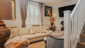 En stue med en beige sofa, et træsofabord, en grå lænestol, et træsidetæppe, en lampe og et billedramme med et billede af en tyr på væggen.
