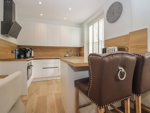 Une cuisine moderne avec des meubles blancs, un plan de travail en bois, un évier et une horloge au mur.