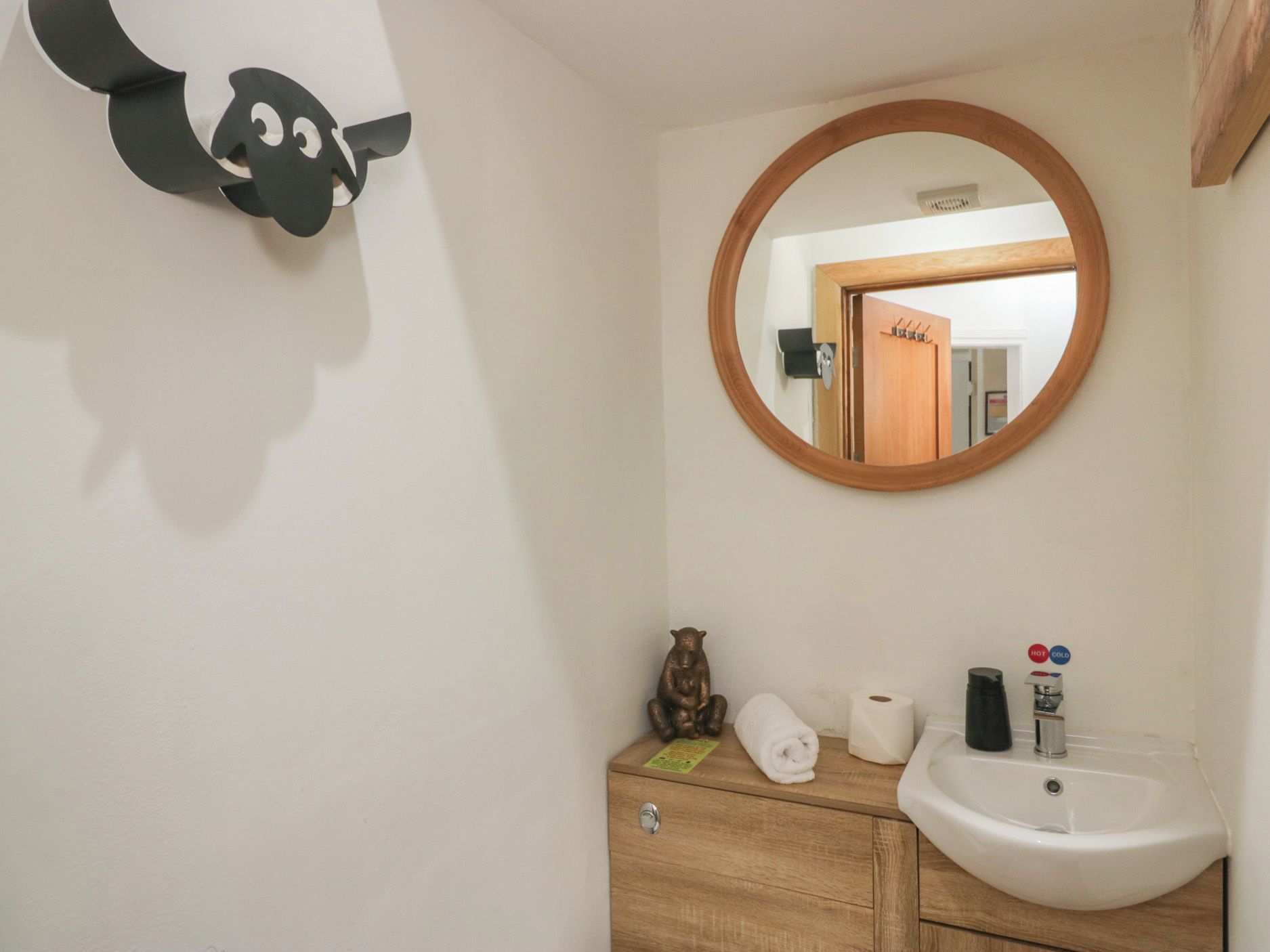 Un baño con tocador de madera, un lavamanos blanco, un espejo y un dispensador de papel higiénico en la pared.