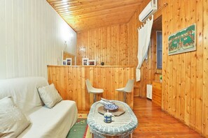 Une pièce chaleureuse avec un décor intérieur en bois, un canapé, deux fauteuils, une petite table avec un bol et une tasse, et un tableau accroché au mur.