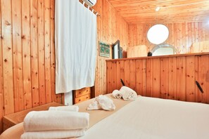 A wooden-paneled room with a bed, towels, a small table, and a mirror.