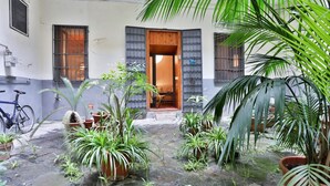 A courtyard with potted plants, a wooden door, and a bicycle. - GuestHost - Cozy 45 sqm apartment, perfect for 2 people, located on the ground floor of a historic building (1 step to access). A stone's throw from Spaccanapoli (in the restricted traffic zone), the property is ideal for those who want to fully experien (Naples)