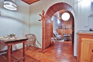 Un intérieur en bois comprenant une table à manger, une chaise en osier et un coin salon confortable agrémenté de coussins.