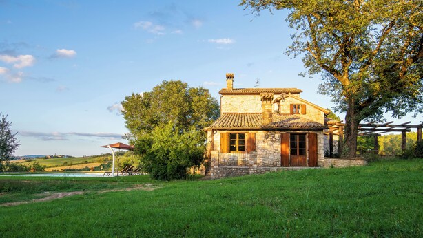 Una casa de piedra con techo de tejas, rodeada de hierba verde exuberante y árboles.