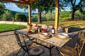 An outdoor dining area with a stone table, metal chairs, and a view of the countryside.