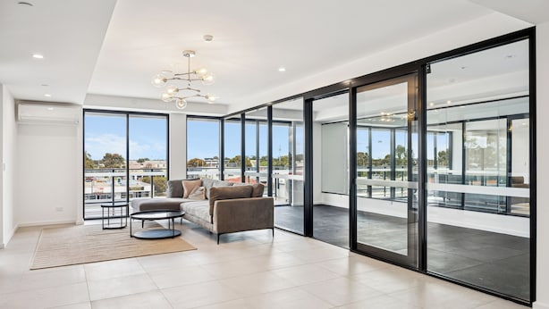 A spacious living area with a large window, a sofa, a coffee table, and a chandelier. - Luxury 2 Bedroom Walk to Transport and Shopping (Cannington)
