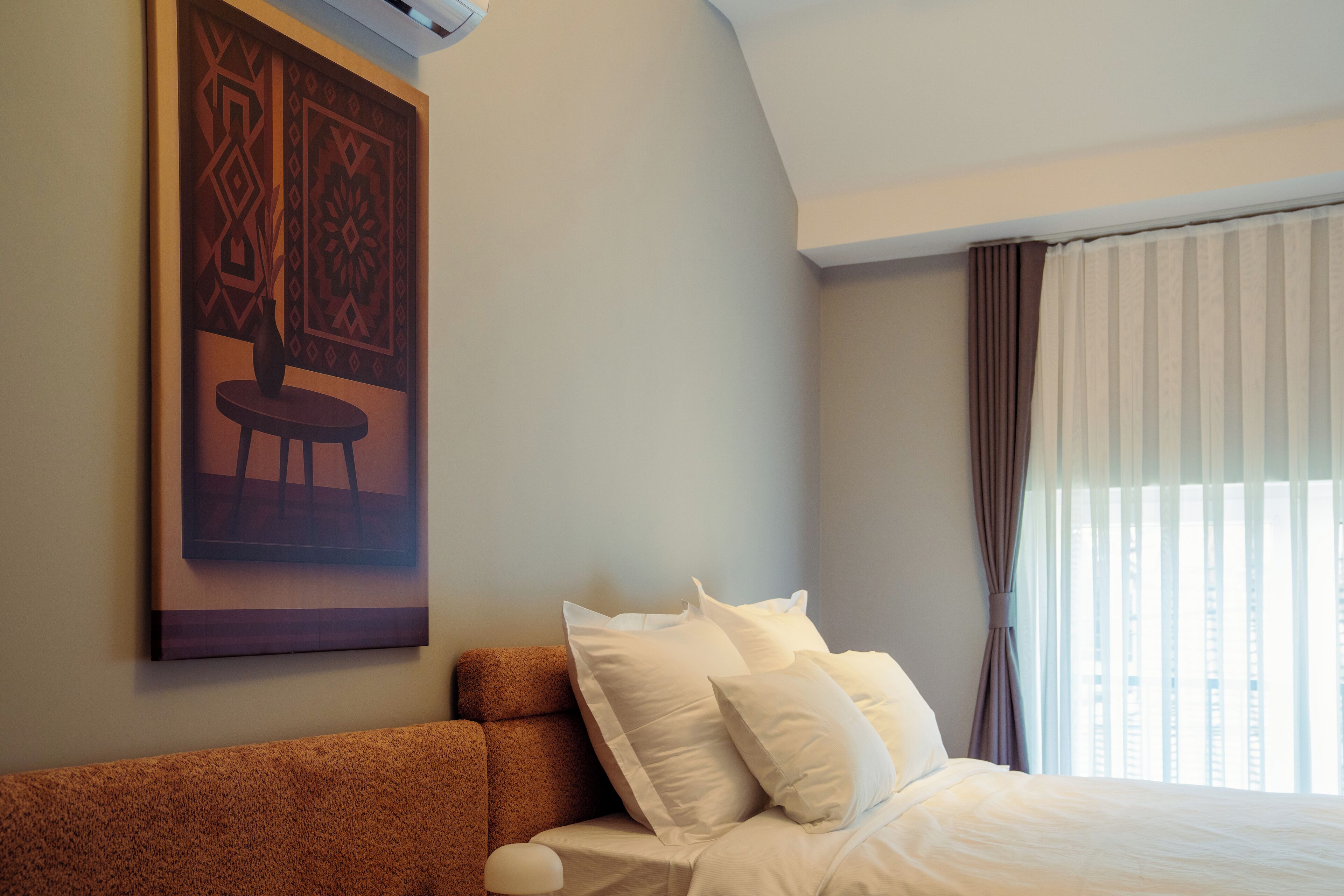 Ein Hotelzimmer mit einem großen Bett, einem braunen Kopfteil, einem Wandbild und einem Fenster mit Vorhängen.