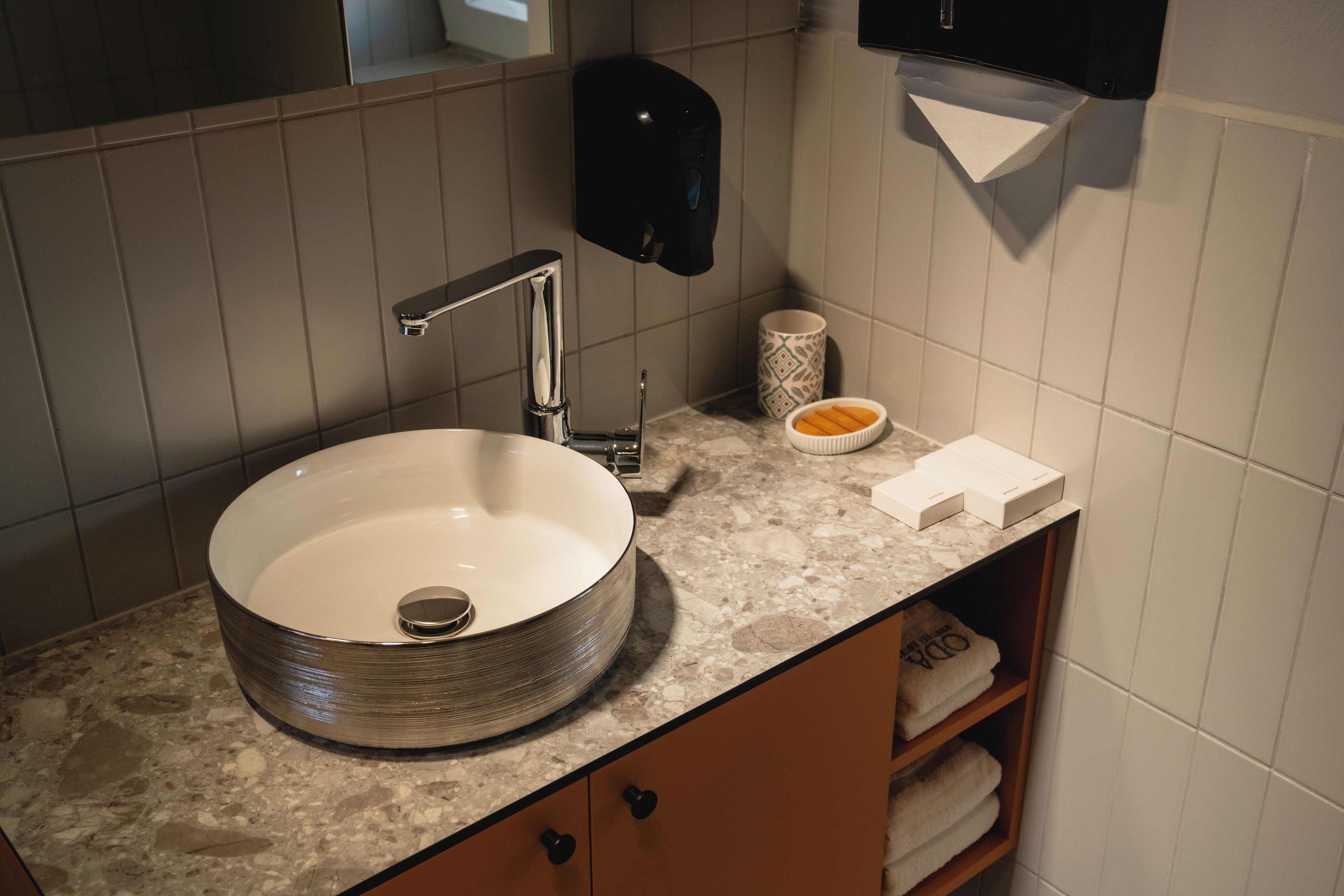 A bathroom with a round sink, a soap dispenser, a towel rack, and a marble countertop.