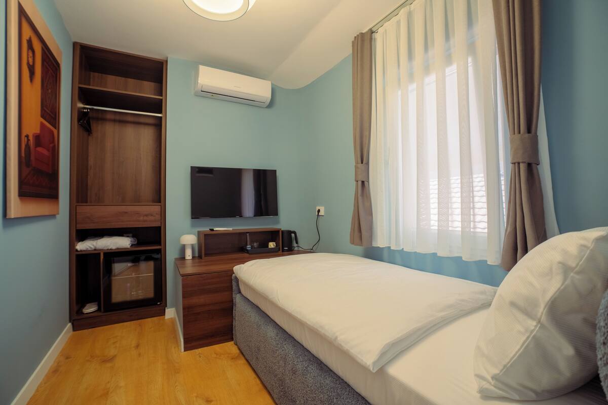 Un dormitorio con cama, televisión, armario y ventana con cortinas.