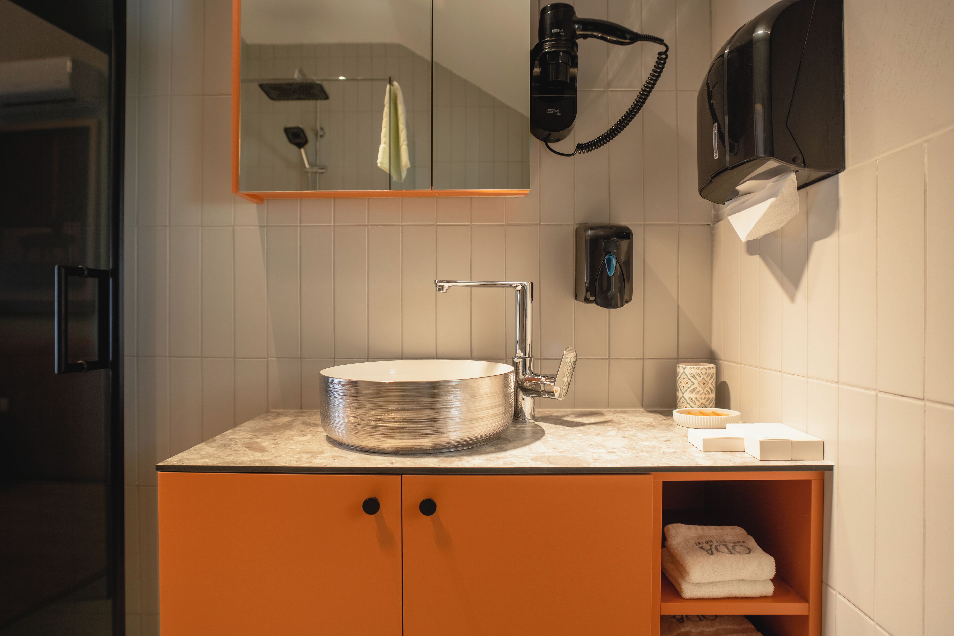 A modern bathroom with a round sink, a towel rack, a hairdryer, and a soap dispenser.