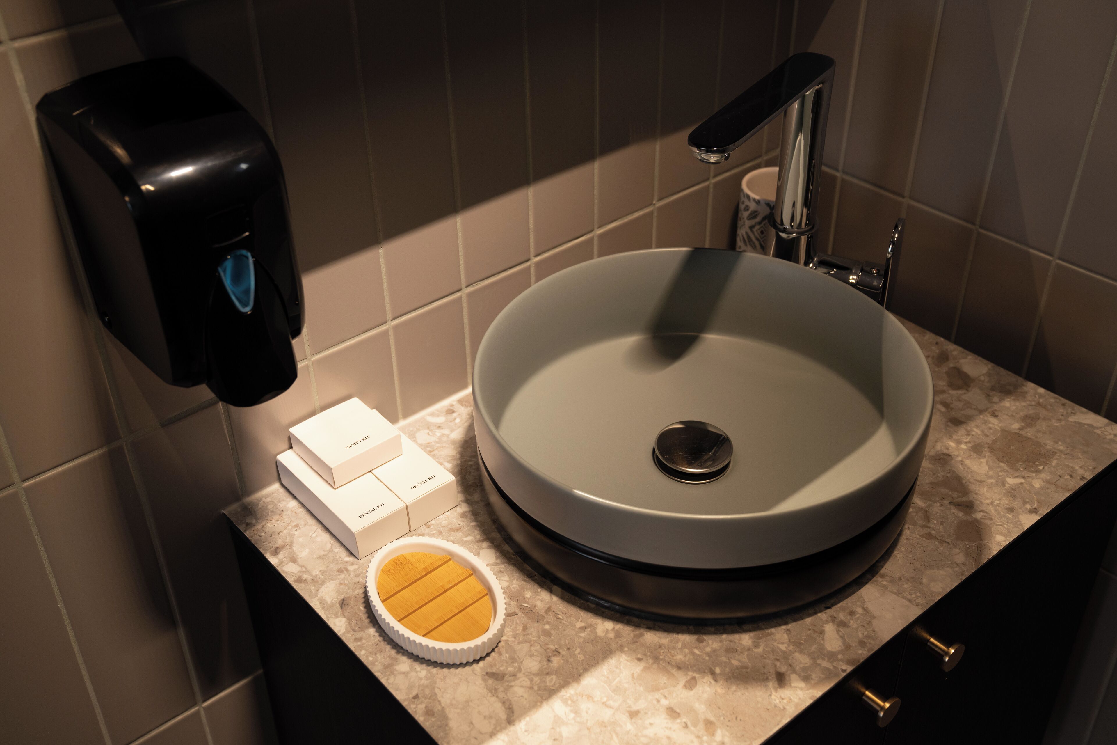 A bathroom with a round sink, a soap dispenser, and a small container on the counter.