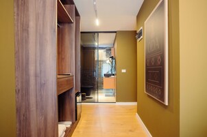 Un pasillo con suelo de madera, una puerta de cristal que da a un baño y un cartel en la pared.