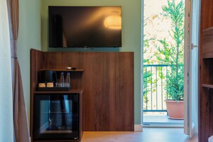 Una habitación con una televisión de pantalla plana montada en la pared, un mueble de madera con vitrina de cristal y una planta en el balcón.