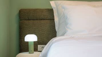 Una cama bien hecha con sábanas blancas, un cabecero verde con textura y una lámpara de noche blanca.