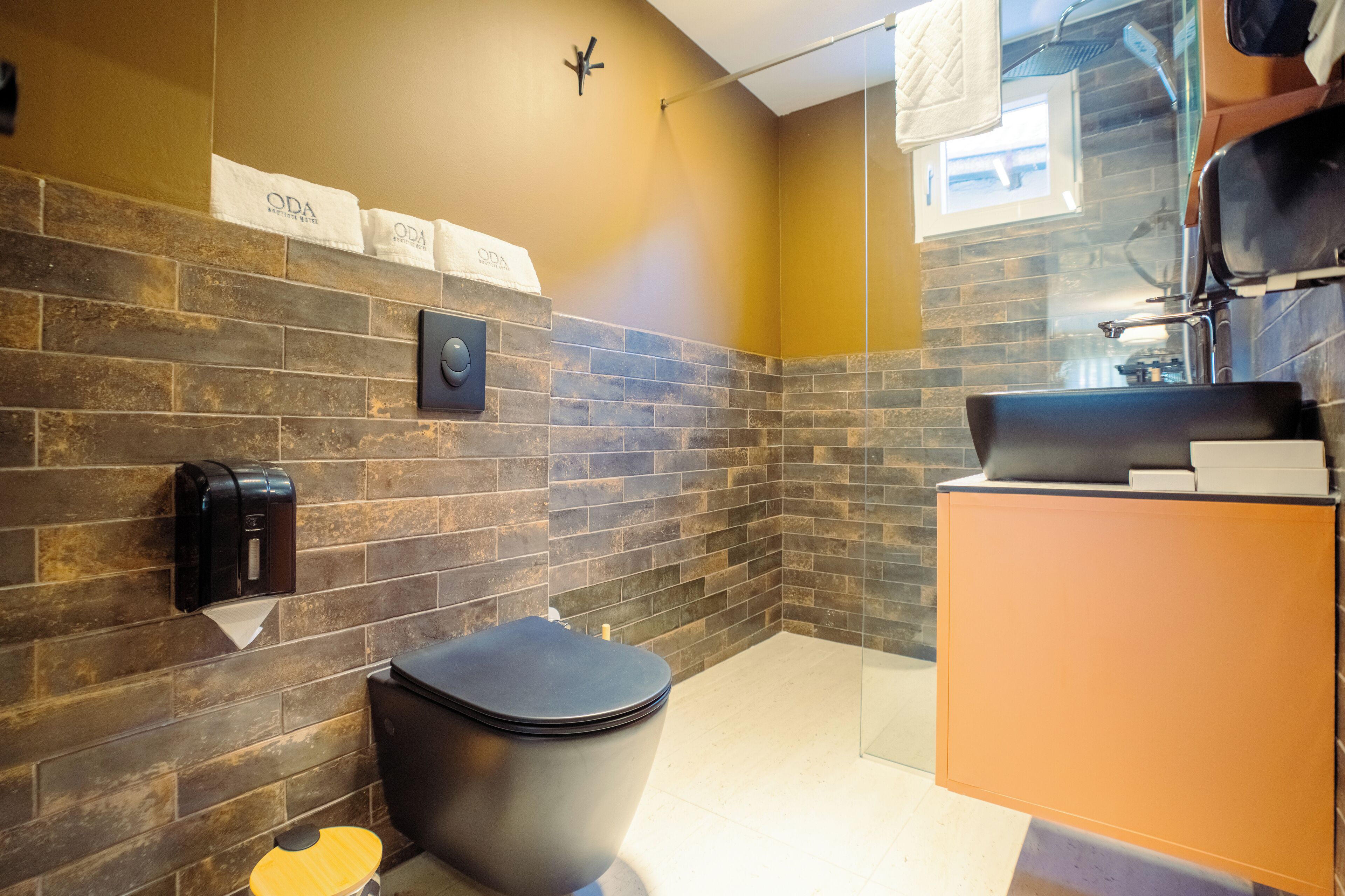 A modern bathroom with a black toilet, a hand dryer, and a towel rack with 'ODA' towels.