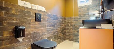 A modern bathroom with a black toilet, a hand dryer, and a towel rack with 'ODA' towels.