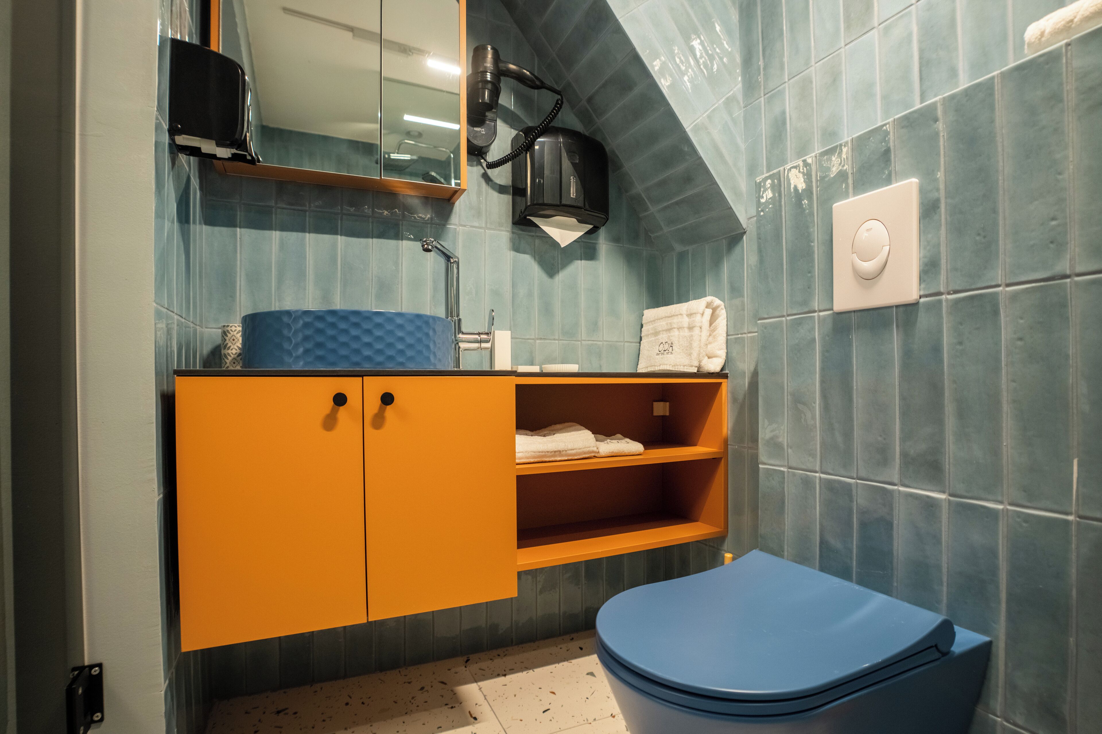 A bathroom with a blue toilet, an orange vanity with a mirror, and a towel rack.