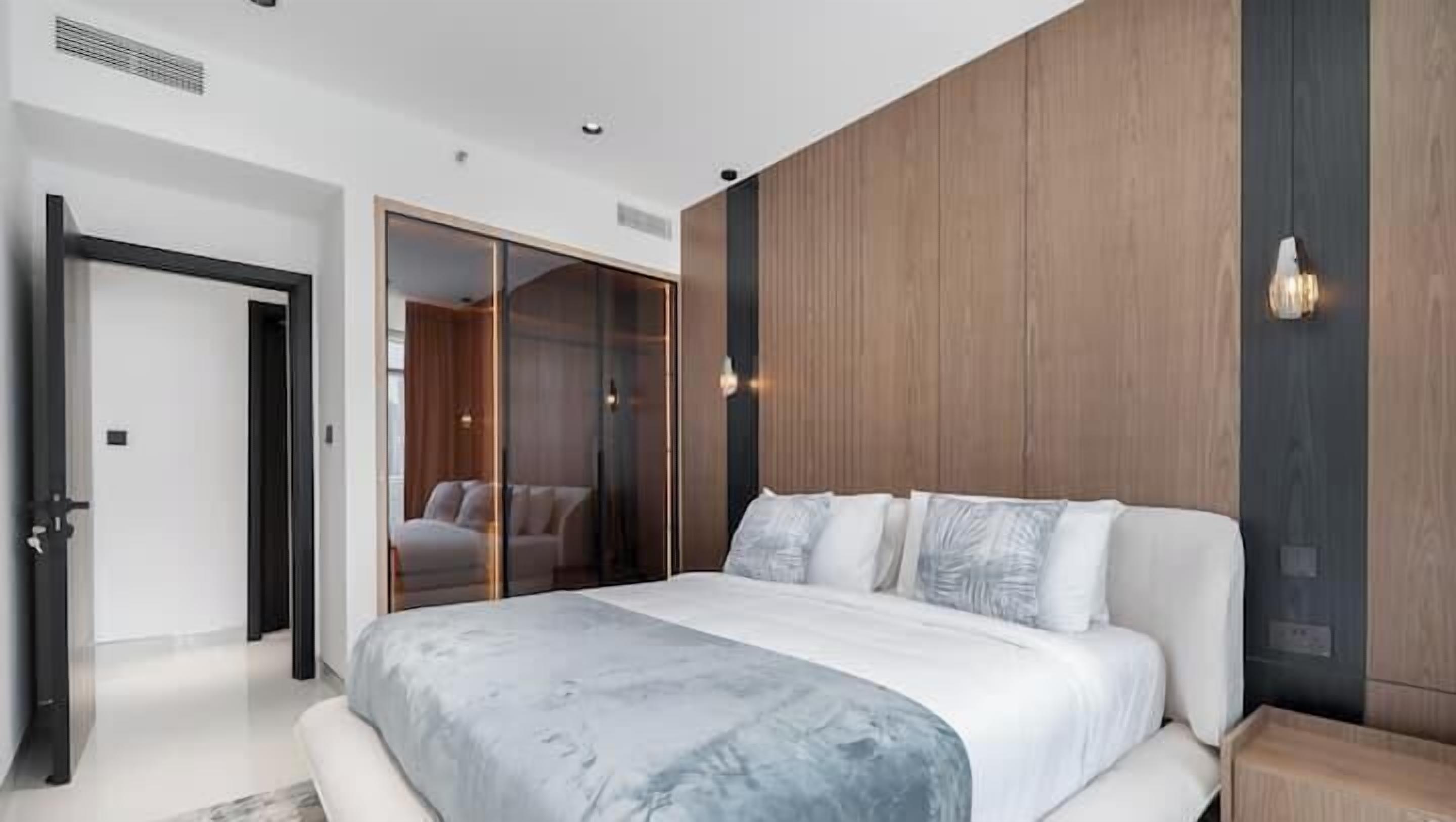 A modern bedroom with a large bed, a walk-in closet, and a wooden accent wall.