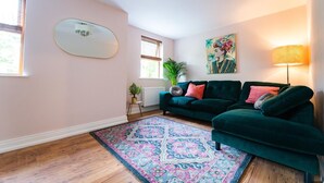 Un salon avec un canapé vert, un tapis à motifs, un tableau et une lampe.