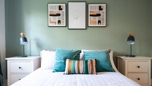 Une chambre à coucher avec un lit, deux tables de chevet et trois œuvres d’art encadrées accrochées au mur.