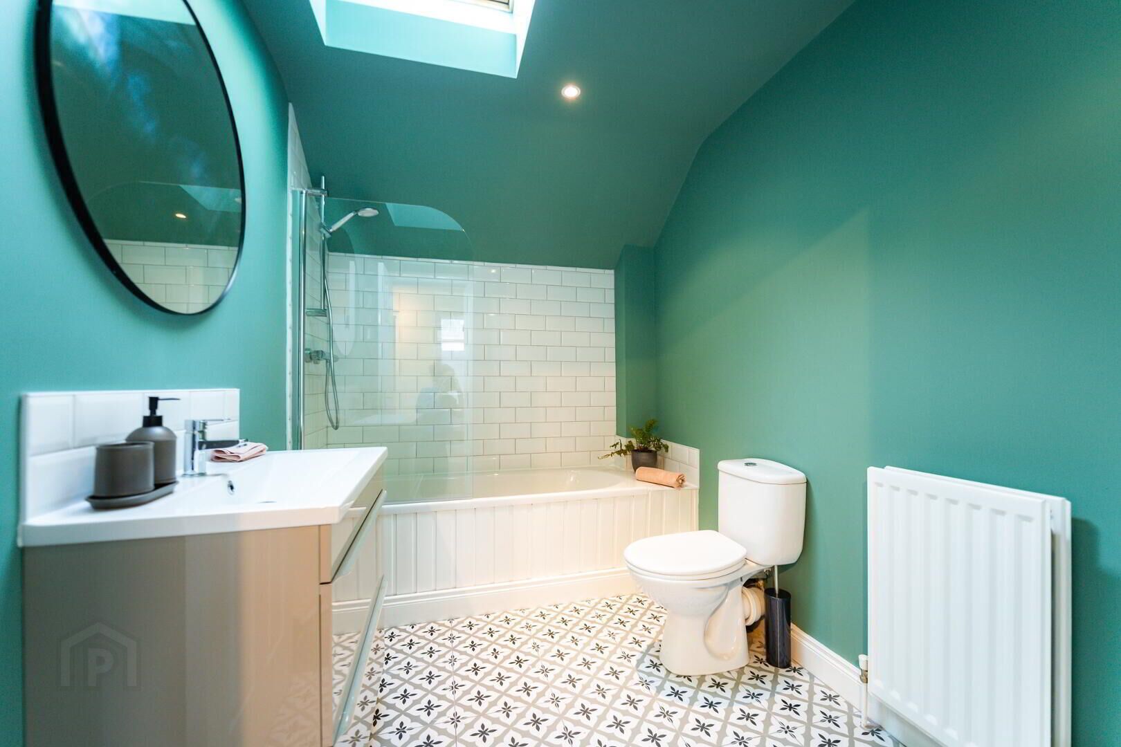 A bathroom with a shower, toilet, and sink, featuring white tiles and a teal wall.