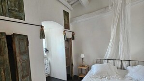 A bedroom with a large bed, a wooden wardrobe, and a small bedside table with a lamp.
