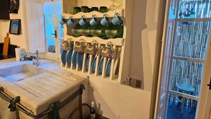 A bathroom with a large sink, a mirror, and a shelf with various bottles and glasses.