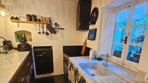 A compact kitchen with a built-in dishwasher, a sink with a window view, and a shelf with kitchen utensils.