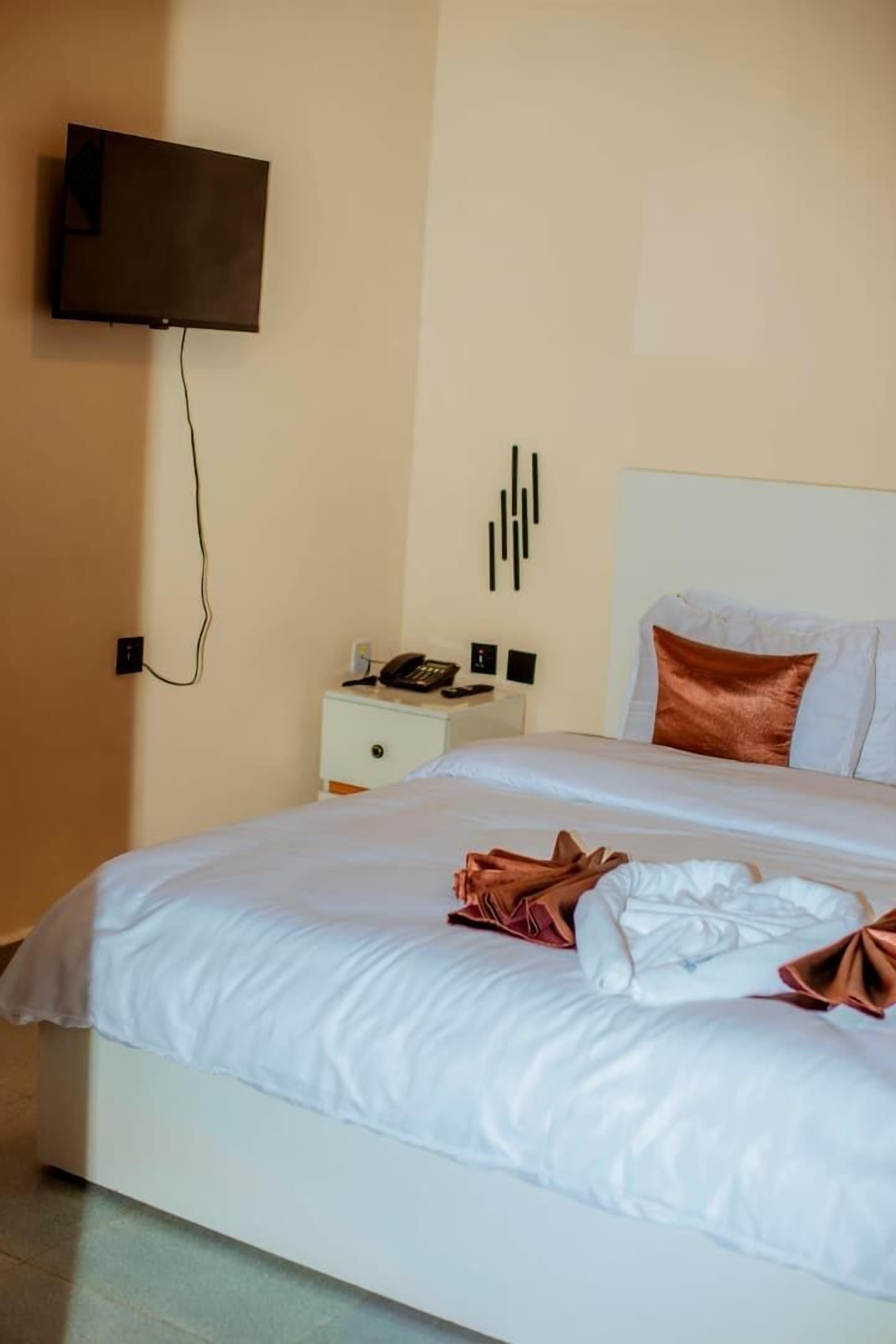 Ein Hotelzimmer mit einem Bett, einem Nachttisch mit Telefon und einem an der Wand montierten Fernseher.