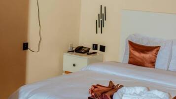 Una habitación de hotel con cama, mesita de noche con teléfono y televisor montado en la pared.