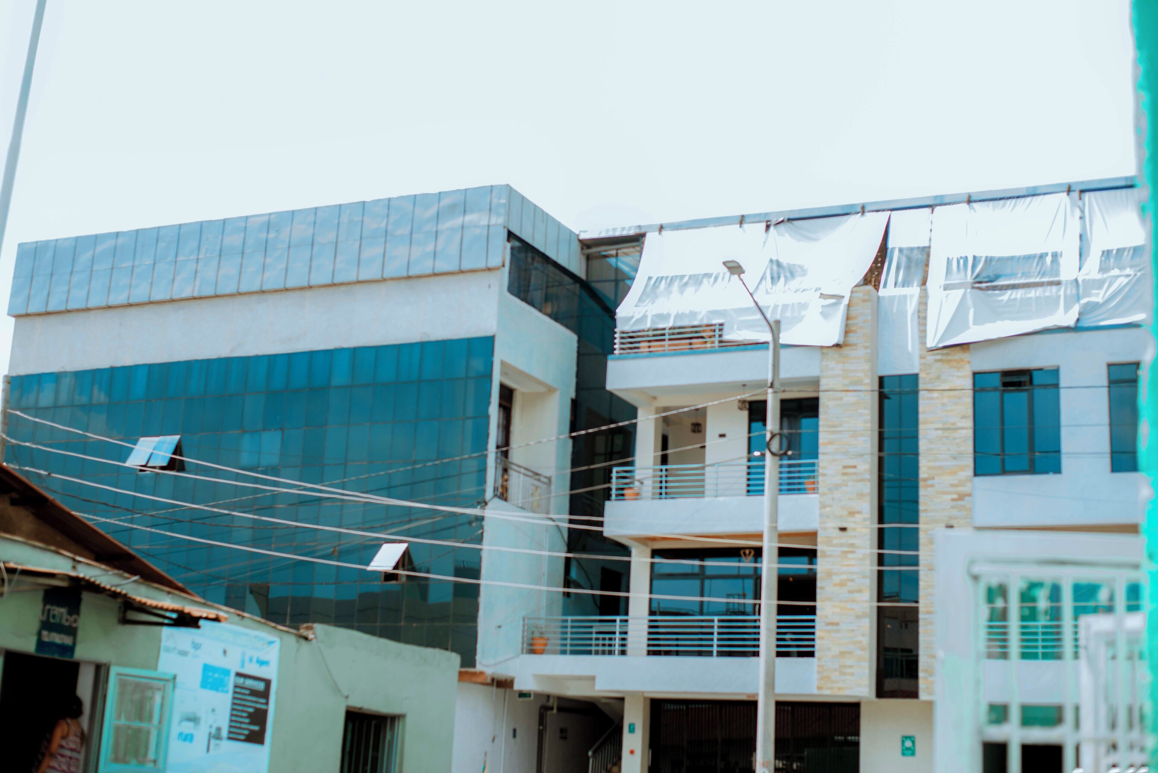A multi-story building with a modern glass facade, a balcony on the second floor, and a visible power line.