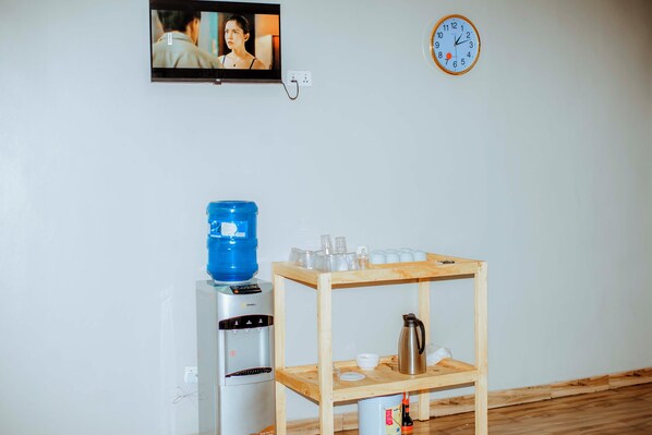 A room with a water dispenser, a coffee maker, and a shelf with cups and glasses.