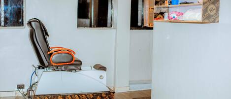 Una habitación con sillón de masajes, un estante pequeño con artículos de aseo y una ventana con persianas.