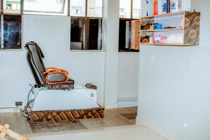 A room with a massage chair, a small shelf with toiletries, and a window with blinds. - La Briella Hotel (Gisenyi)