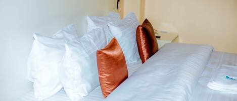 A neatly made bed with white and brown pillows, a white blanket, and a white pillow on the right side.