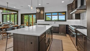 Une cuisine moderne dotée d’un grand îlot central, de meubles de couleur sombre, d’appareils électroménagers en acier inoxydable et offrant une vue sur l’extérieur.