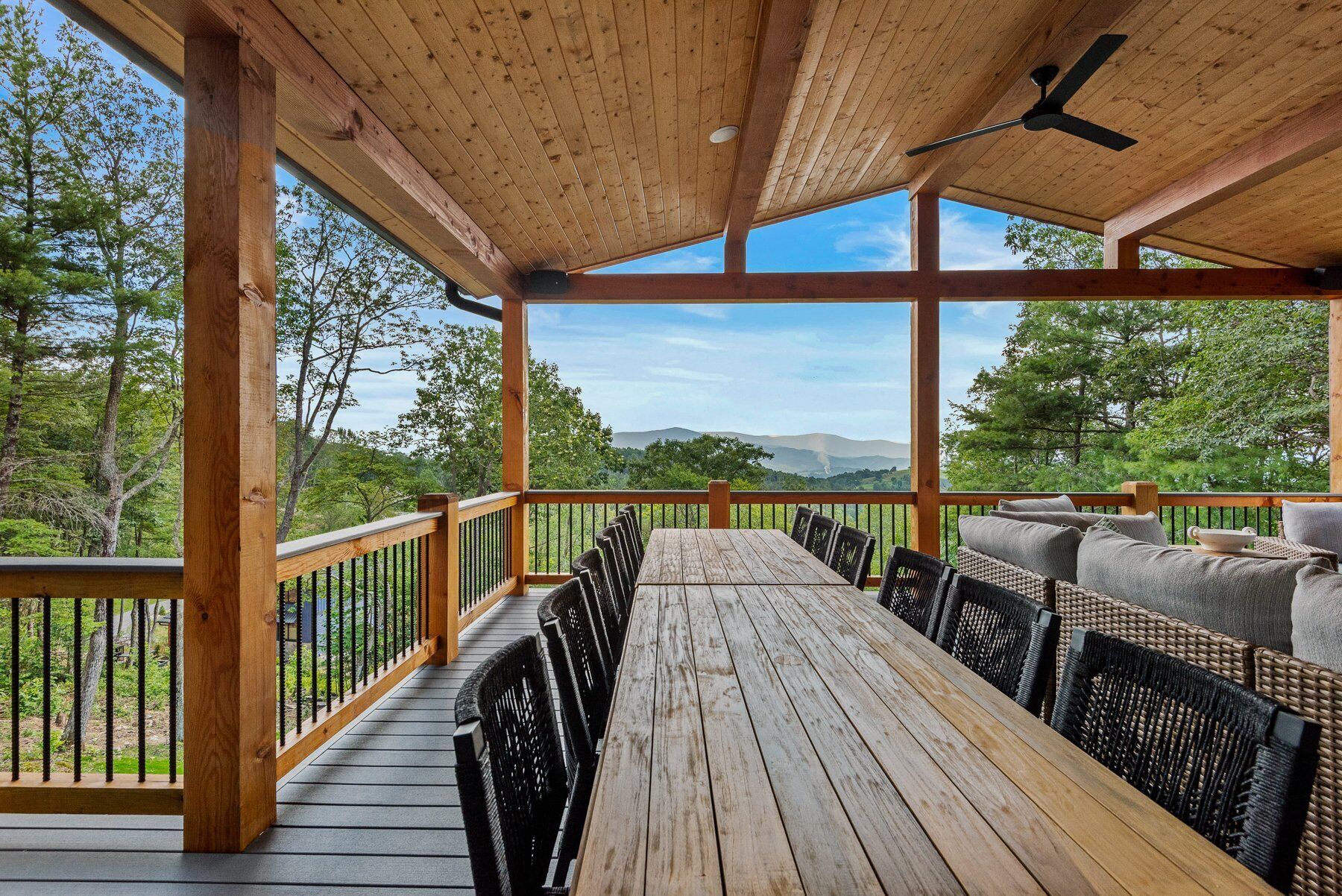 Een houten terras met een tafel en stoelen, met uitzicht op een bebost gebied en verre bergen.