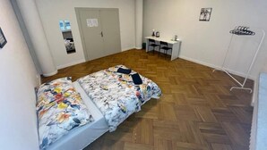 A room with two beds, a desk, chairs, a coat rack, and a door.