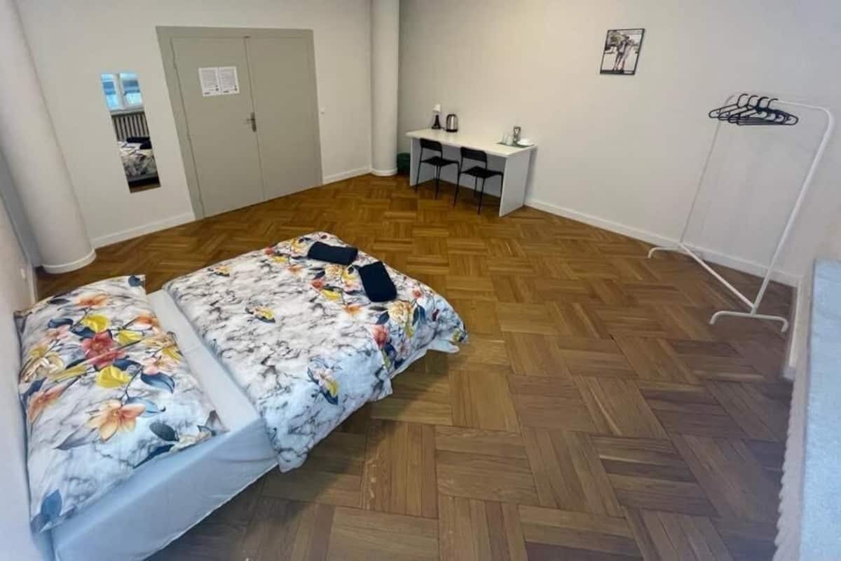 Ein Zimmer mit zwei Betten, einem Schreibtisch, Stühlen, einem Kleiderständer und einer Tür.