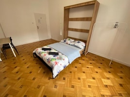 Une pièce avec un lit, un plancher en bois, une porte et une chaise.