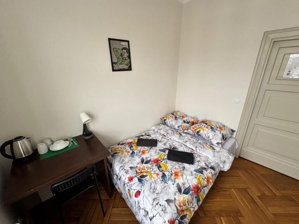 Une petite pièce avec un lit, un bureau et une chaise. Il y a une affiche au mur et une porte sur laquelle est apposée un avis.