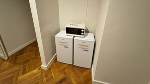 A corner of a room with a microwave on top of a white appliance, possibly a washer and dryer, in a hallway with wooden flooring.