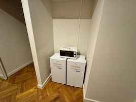 Un coin de pièce avec un four à micro-ondes posé sur un appareil blanc, qui pourrait être un lave-linge et un sèche-linge, dans un couloir au plancher en bois.