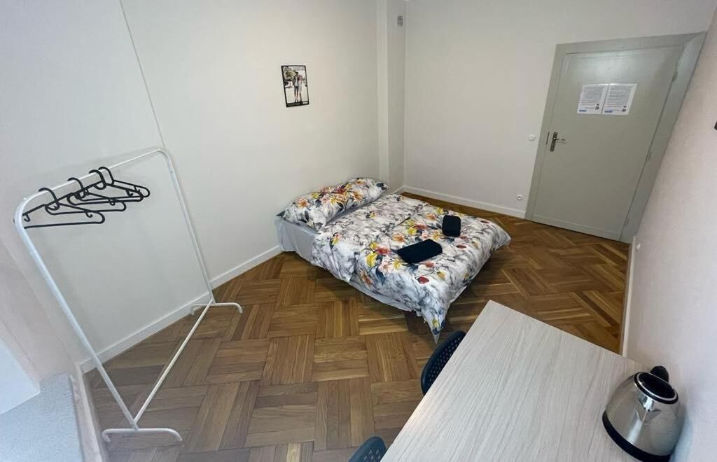 A small, clean room with a bed, a desk, and a kettle.