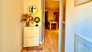 A hallway with a white dresser, a mirror, a vase with dried flowers, and a clock.